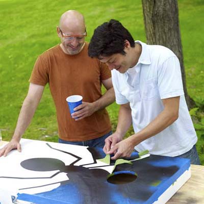 two men removing tape of design for cornhole game board