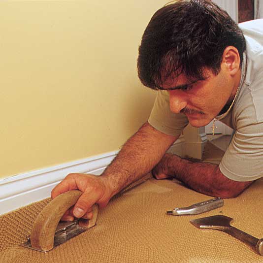 person using a carpet-edging tool to demonstrate how-to install carpet