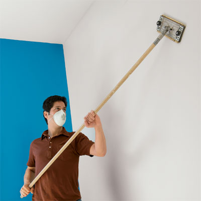 man sanding a wall using a sanding pole and sandpaper