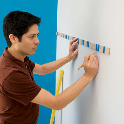 person using a story stick to mark the wall where stripes will be painted