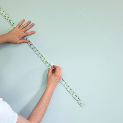 man using yardstick to make chalk grid for wall stenciling