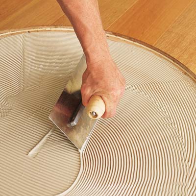 spreading an even layer of wood flooring adhesive into the subfloor area of the circle