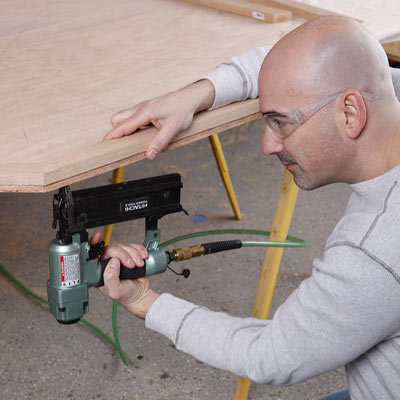 man using nail gun to construct poker table