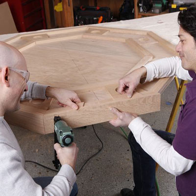 two men attaching apron on poker table