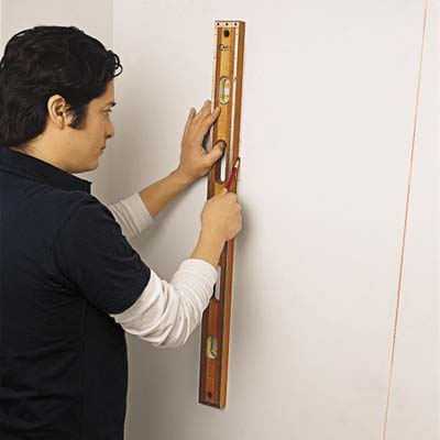 Image of person holding a level to the wall to mark the line of studs, once found with the stud finder.