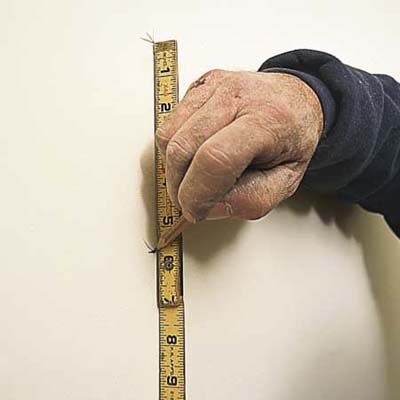 tom silva measuring with a measuring tape, and marking layout line of the wall with a pencil