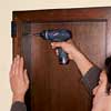 Drive drywall screws through the holes in the side of the cabinet and into the blocking